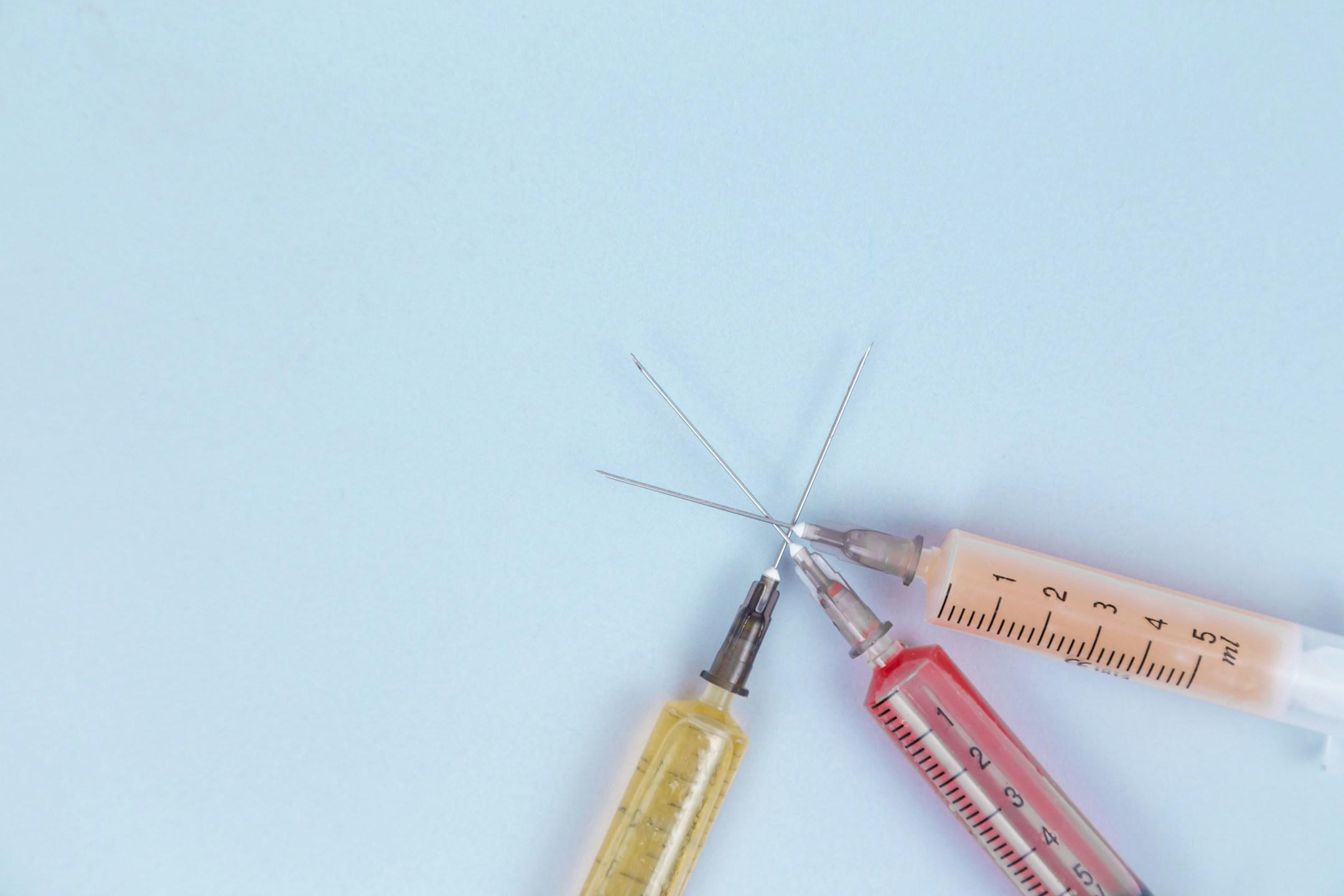 Syringes with different medicines in yellow, red, orange and transparent colors lie on a blue background.