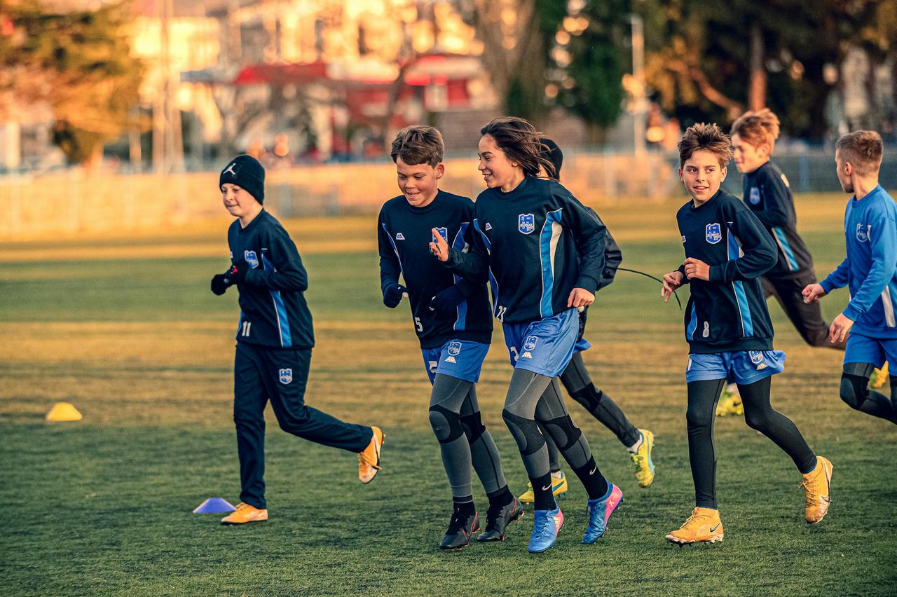 A group of boys running joyfully during a soccer practice session on a grassy field.