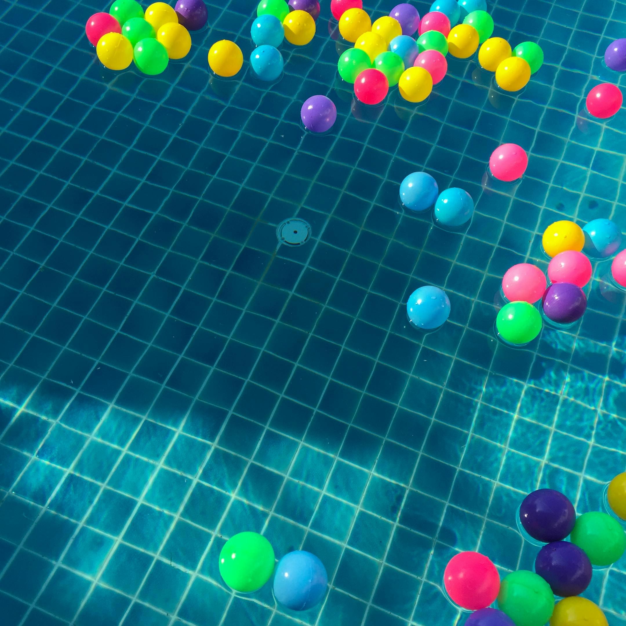 Floating colorful plastic balls in a sunlit swimming pool, creating a vibrant and playful scene.
