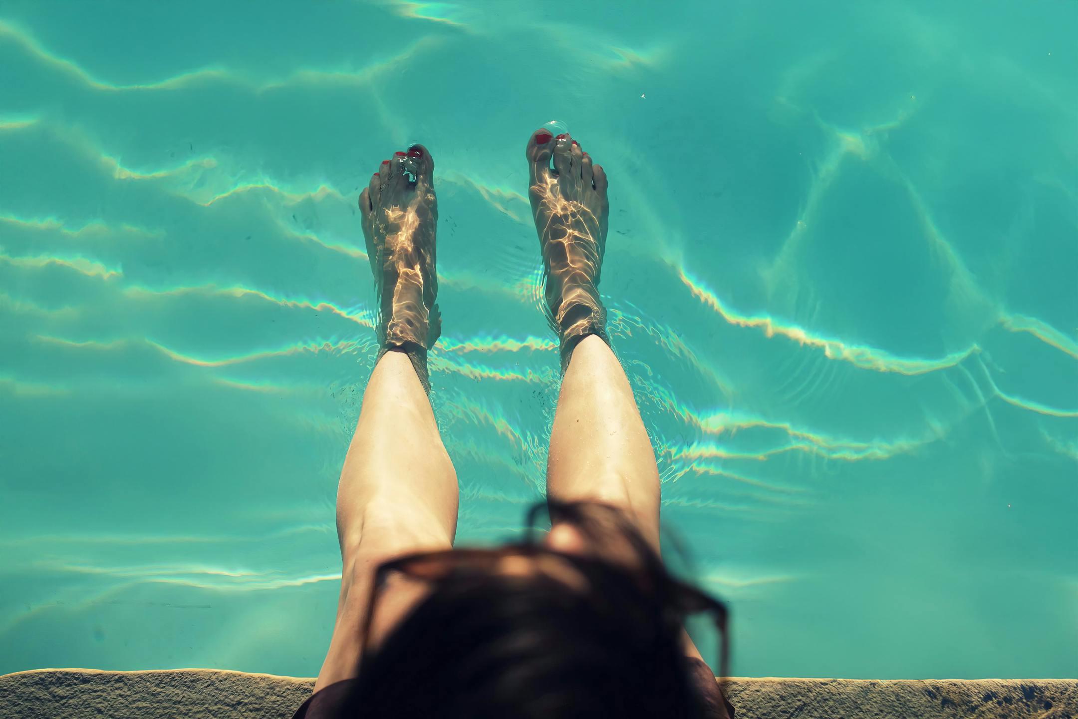 Woman relaxing with feet dipped in a clear pool on a sunny day, capturing a refreshing moment.
