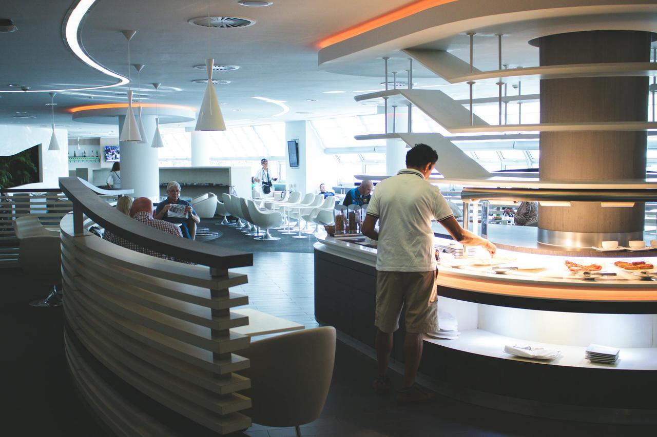 Stylish airport lounge with buffet and seating, featuring sleek interior design and contemporary furniture.