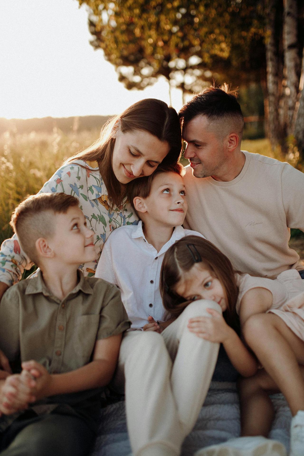 A joyful family of five sitting together, enjoying a warm sunset in the countryside.