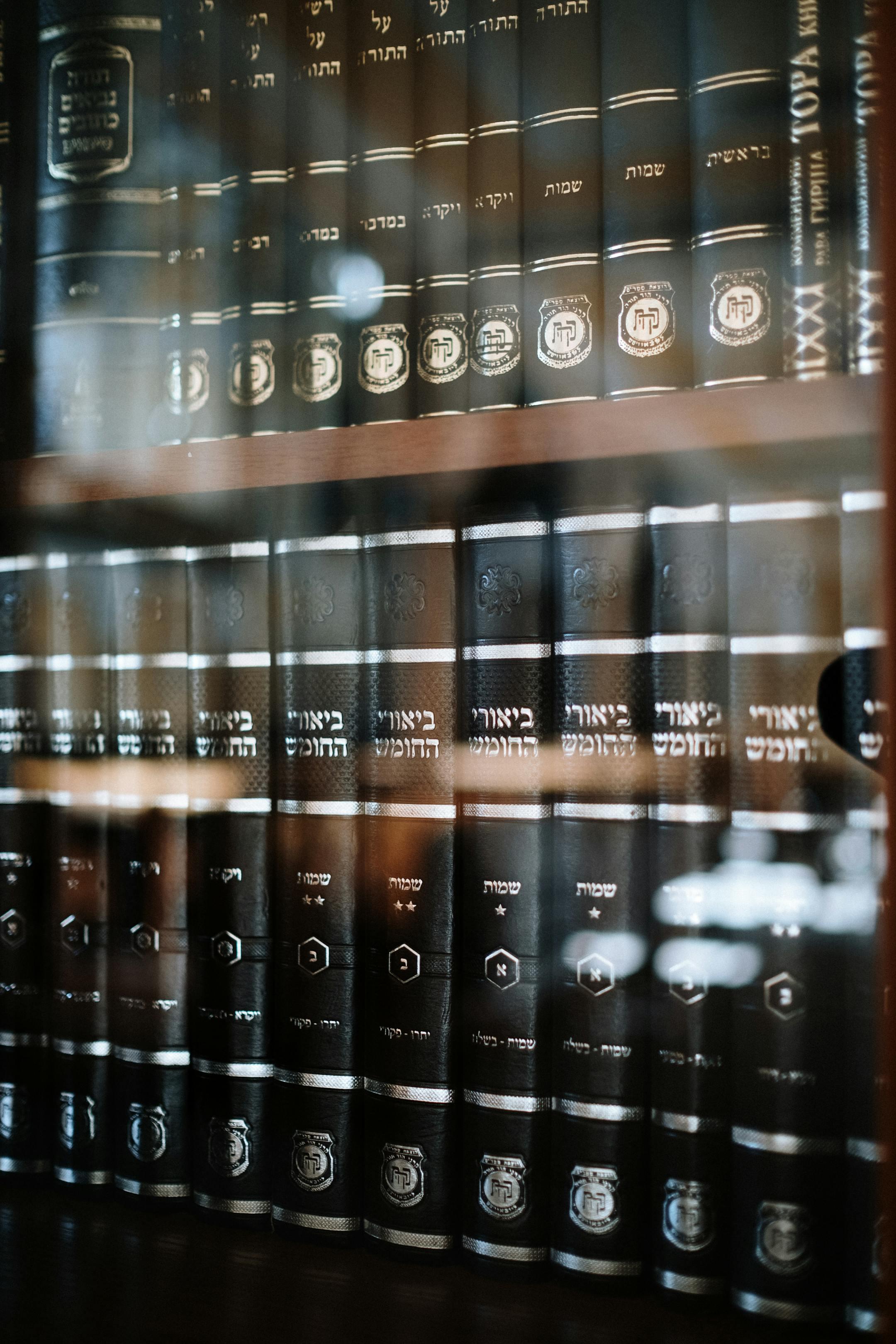 A collection of Jewish religious books neatly arranged on a shelf behind glass.