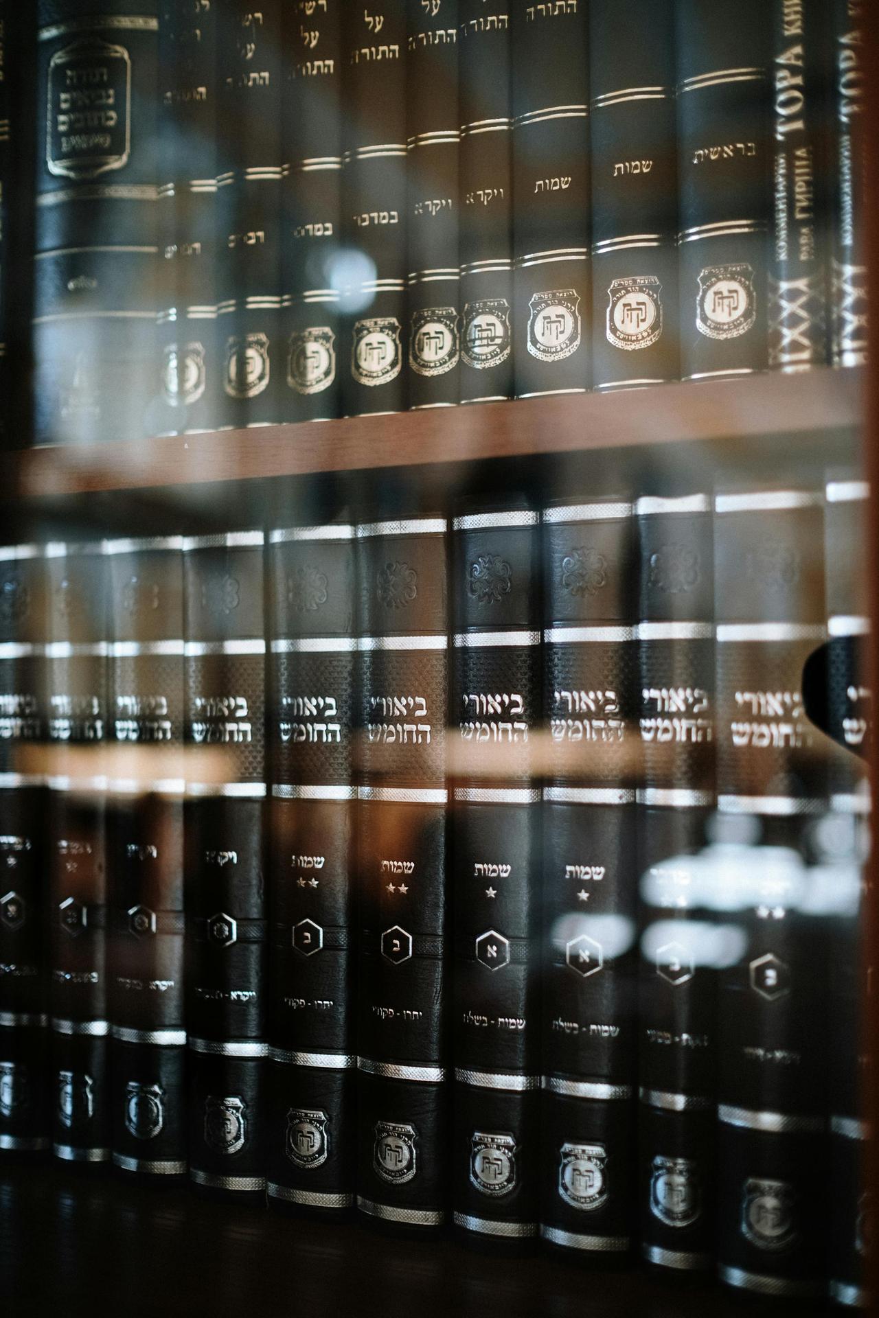 A collection of Jewish religious books neatly arranged on a shelf behind glass.
