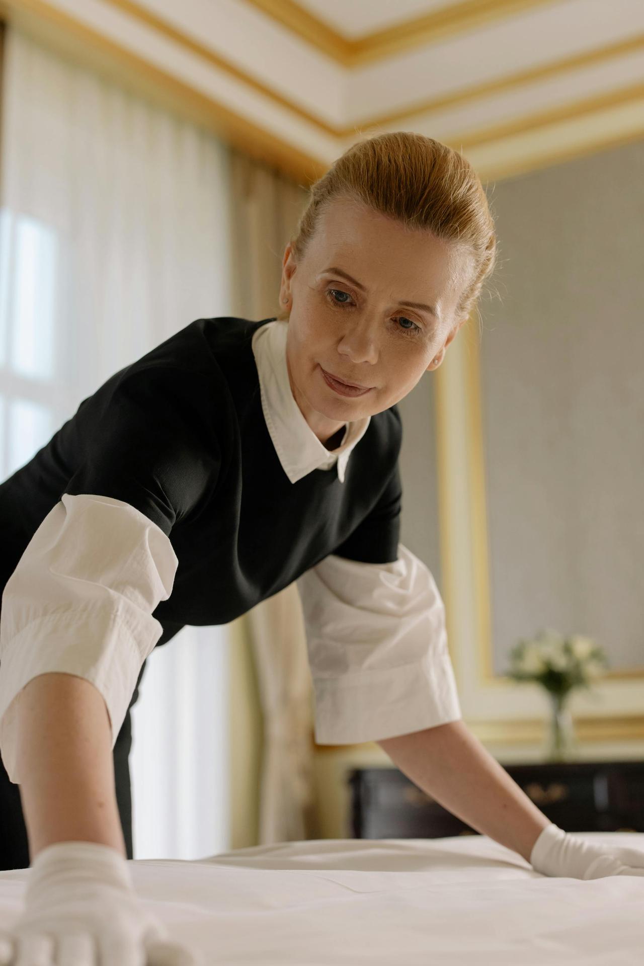 A housekeeper in uniform skillfully arranges bed linen in a luxurious hotel room.