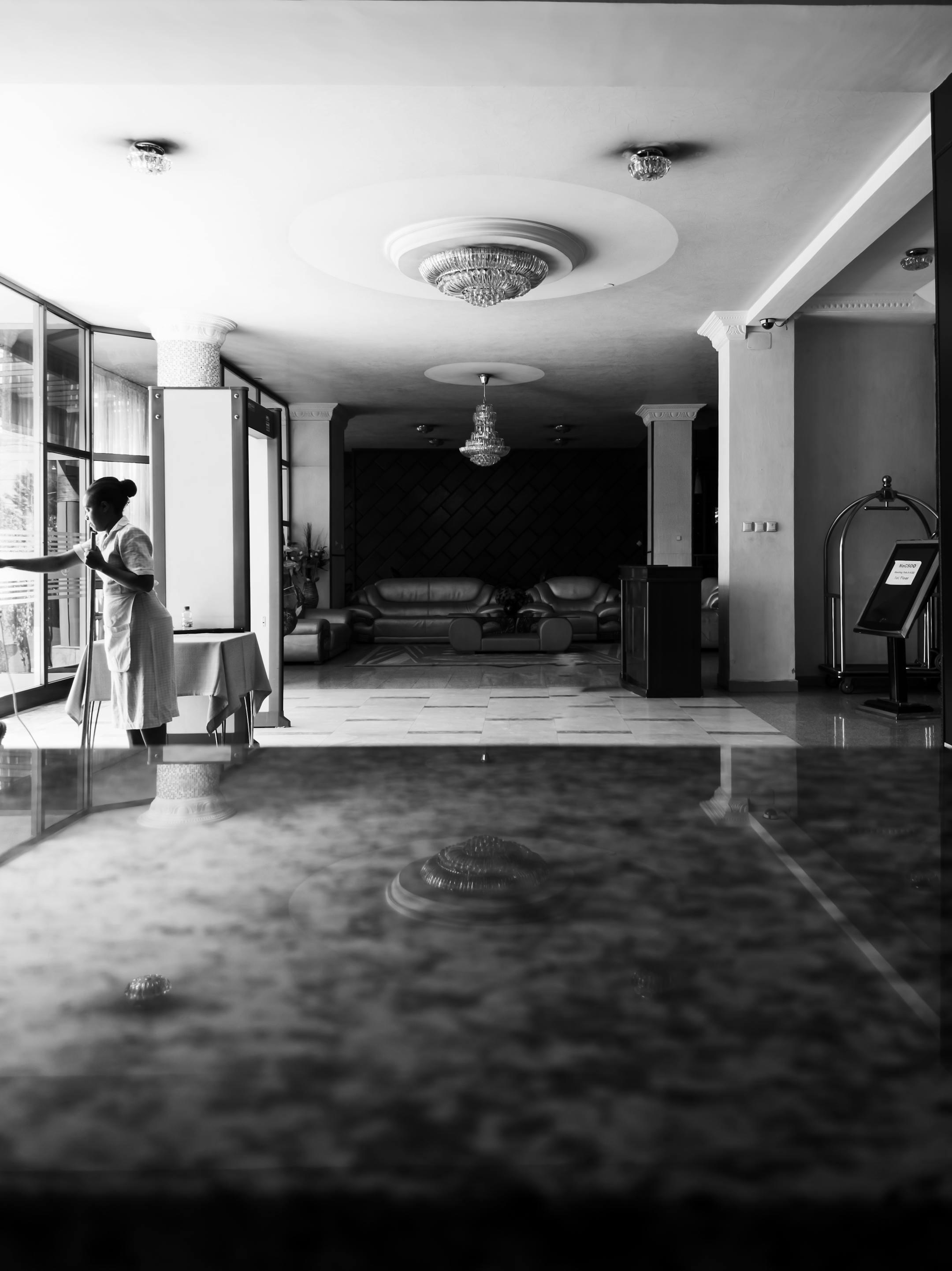 Black and white photo of a housekeeper cleaning a luxury hotel interior, emphasizing elegance and cleanliness.