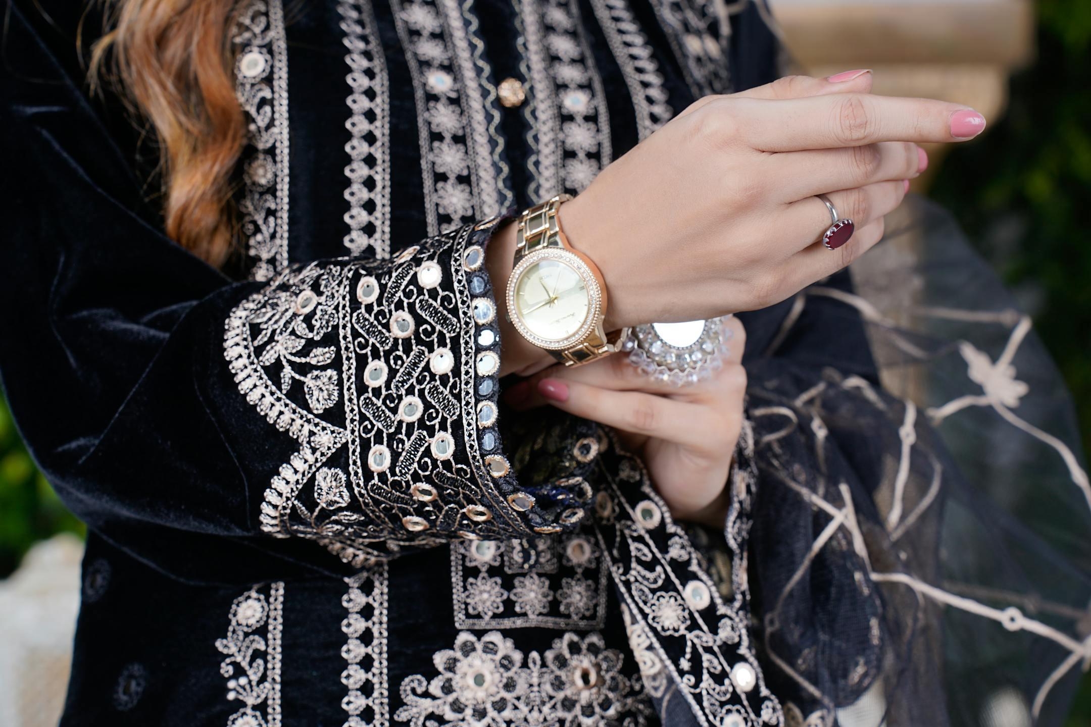 Close-up of a woman in embroidered attire showing jewelry and watch.