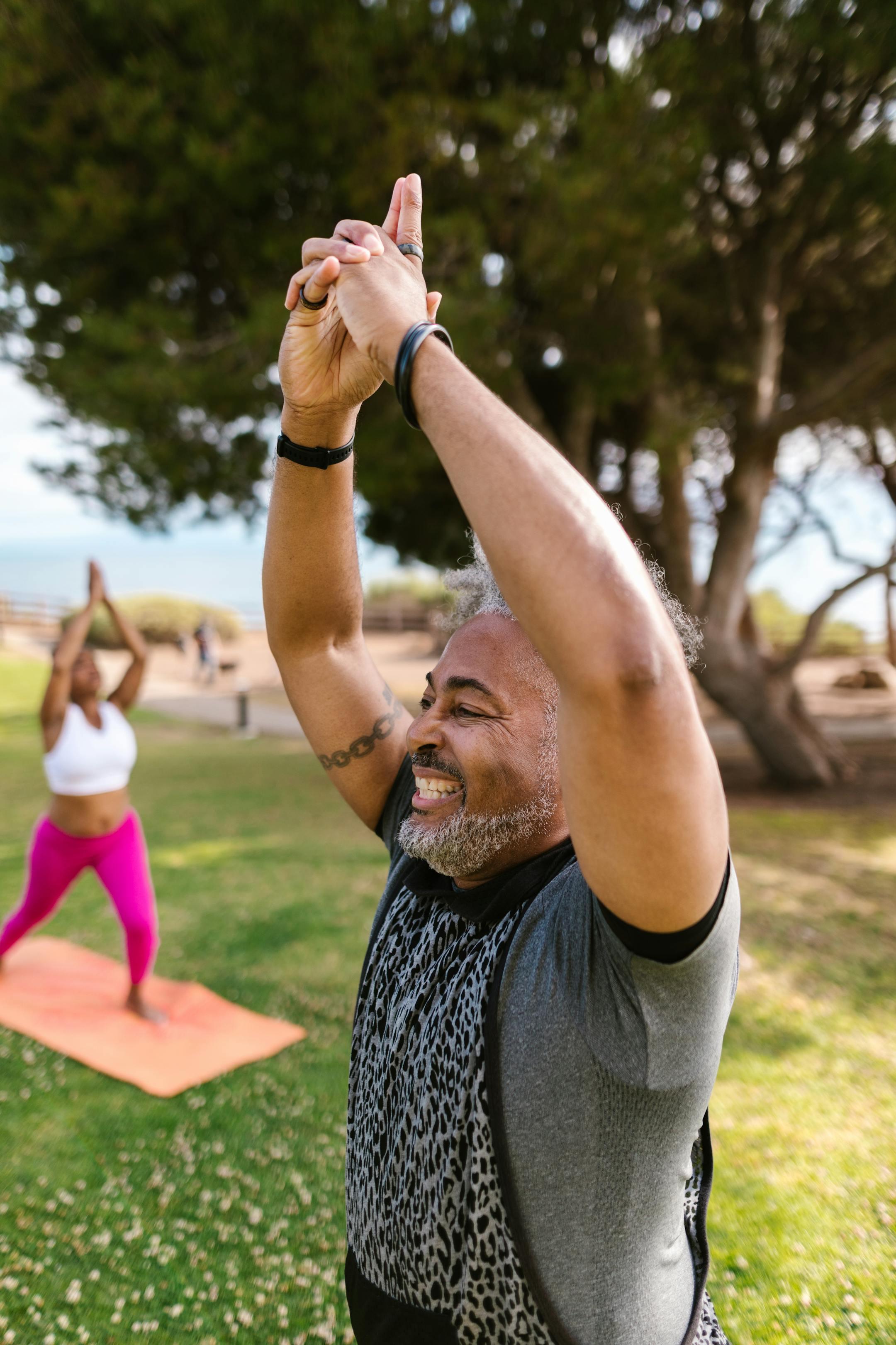 Smiling middle-aged man doing yoga in a park, promoting health and wellness.