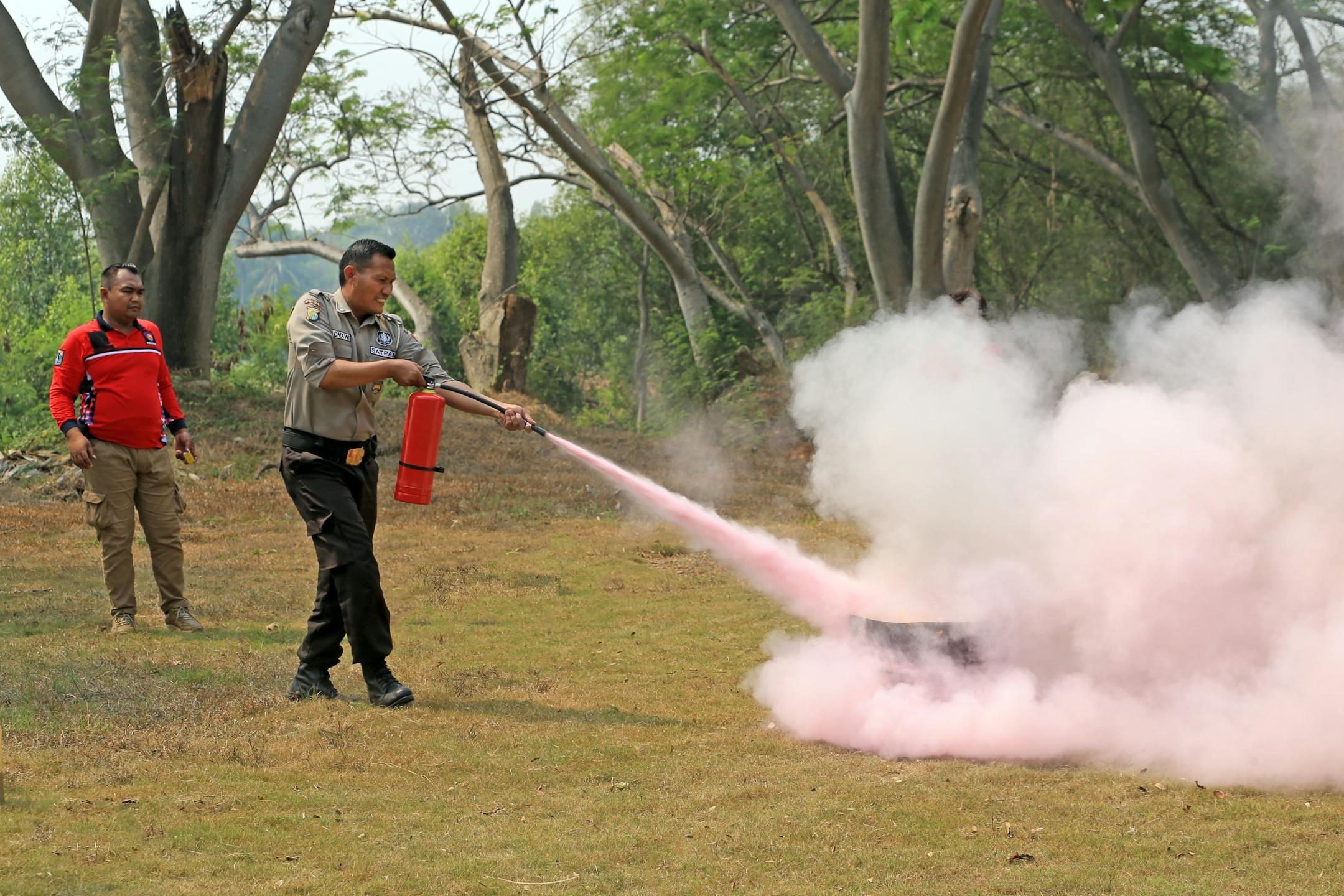 A fire safety officer demonstrates use of an extinguisher during outdoor training, releasing pink smoke.
