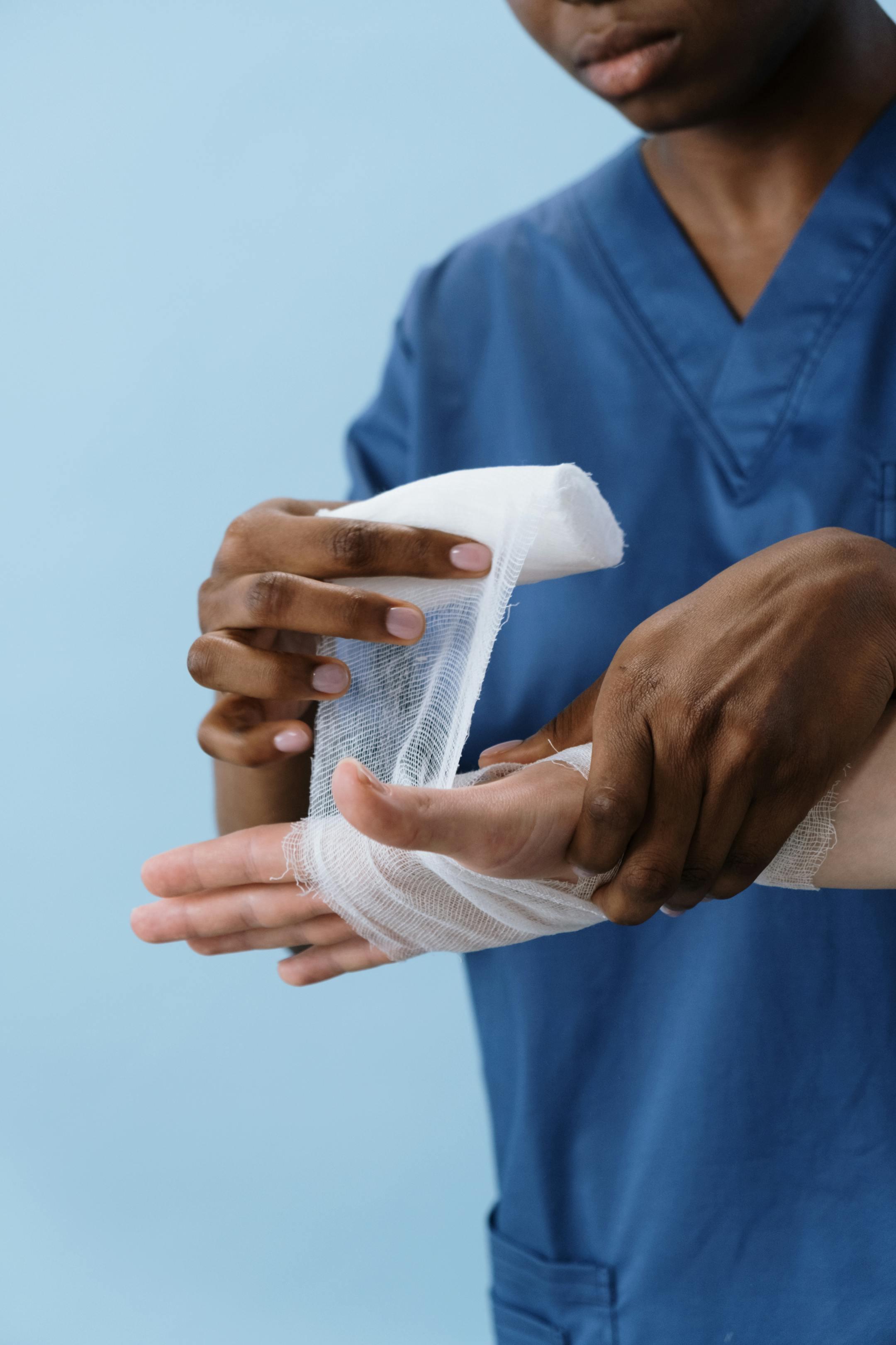 A healthcare professional wrapping a patient's hand with gauze for injury care.