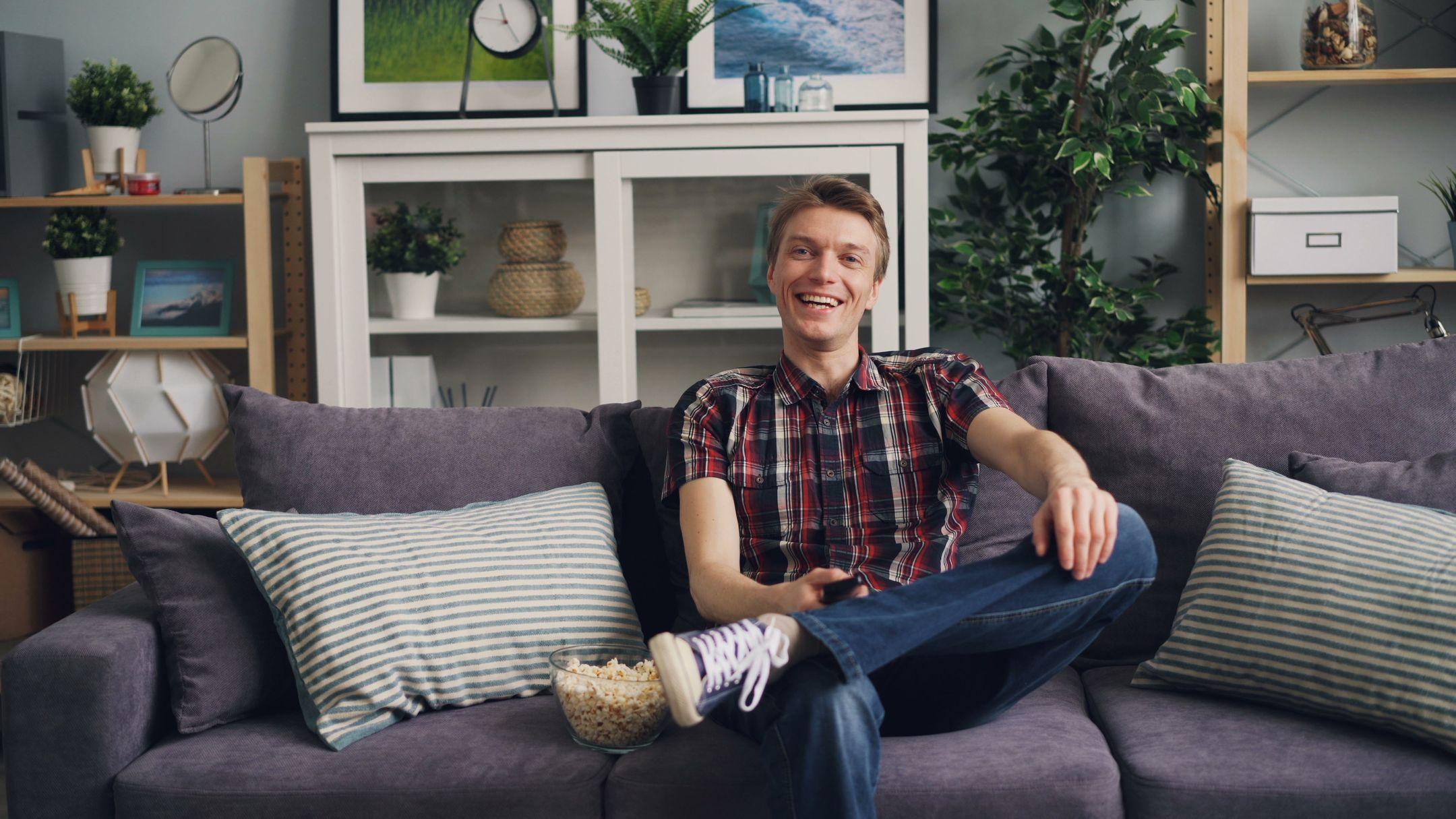 A cheerful man sits on a sofa with popcorn, enjoying his leisure time in a stylish living room.