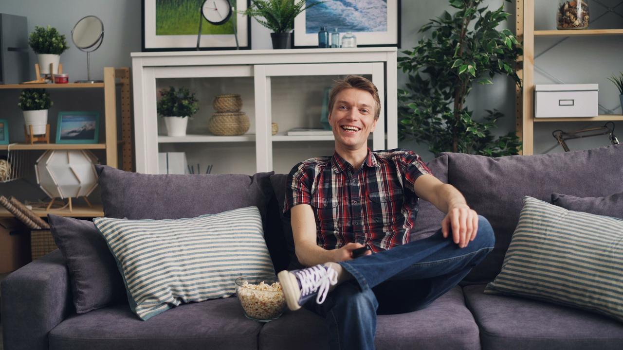 A cheerful man sits on a sofa with popcorn, enjoying his leisure time in a stylish living room.