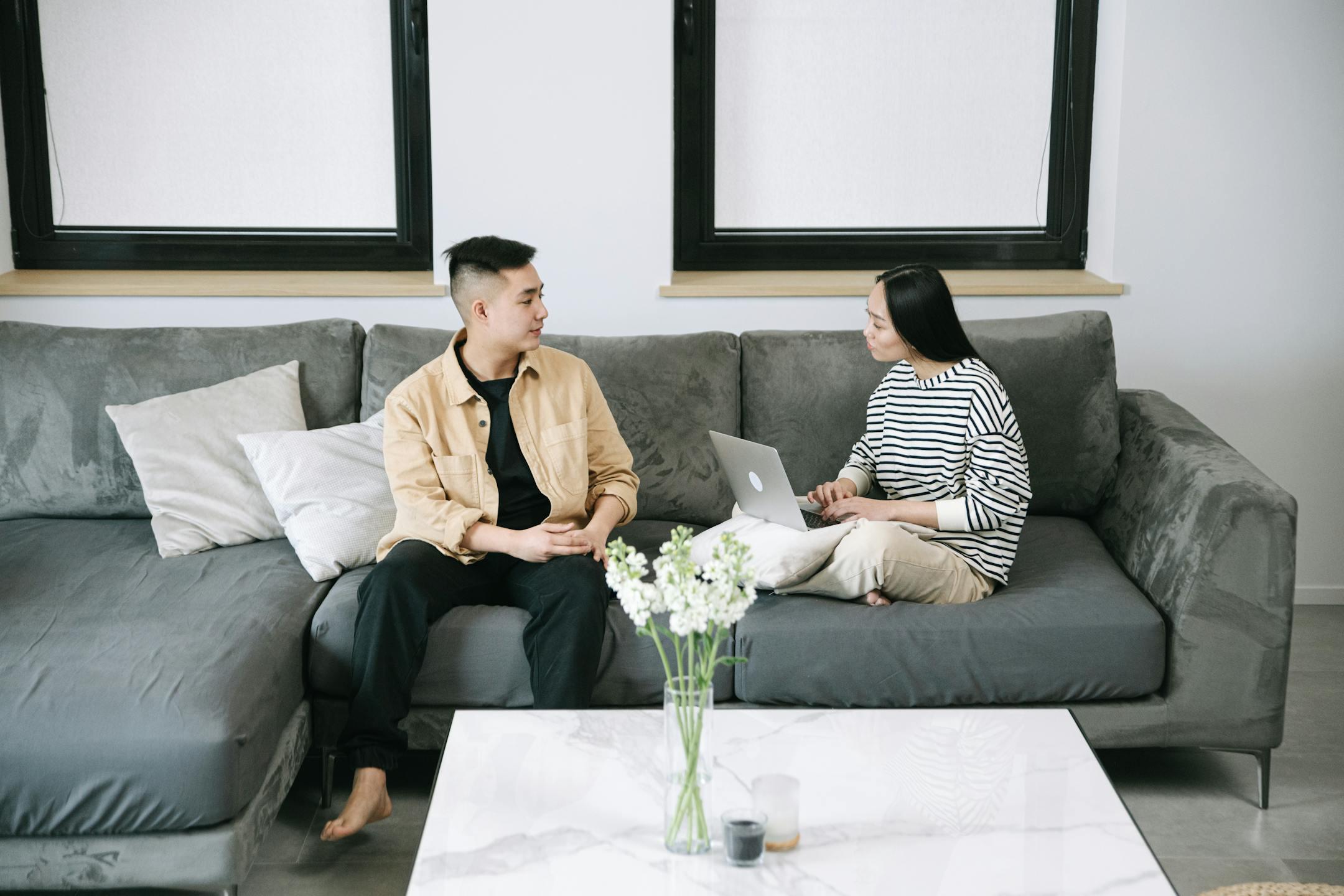 Man and woman discussing while working on a laptop in a stylish living room, creating a warm, casual atmosphere.
