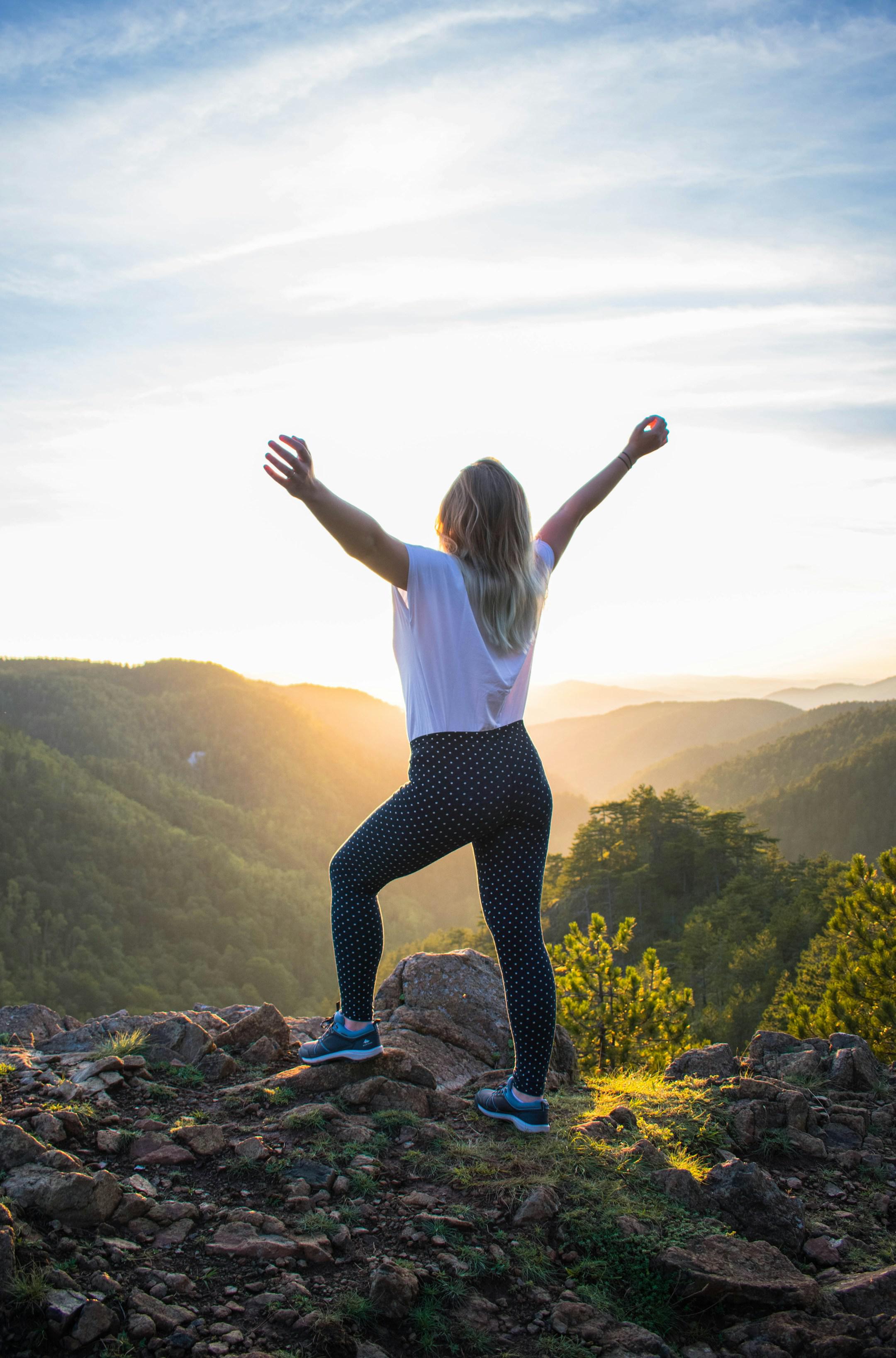 A woman standing in front of the sunset, with arms wide open, soaking energy, feeling happy, invigorated, motivated. Divčibare, Serbia.