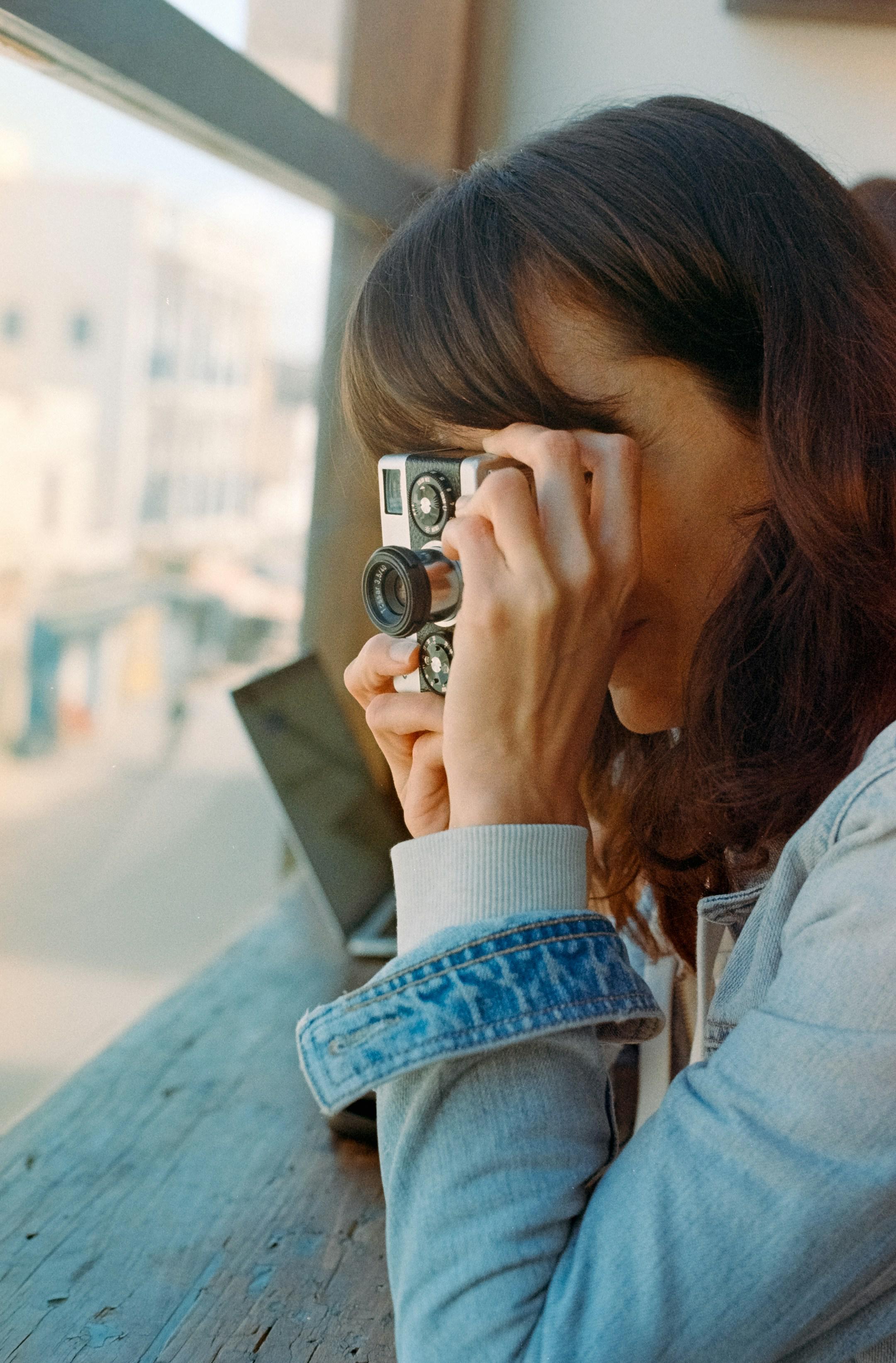 An analog photo of a woman taking a photo with her old Rollei camera. Taken on 35mm film with a Canon AE1 Program and then digitally scanned.