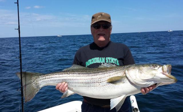 grandpa in black t shirt and hat holding a striped bass he recently caught