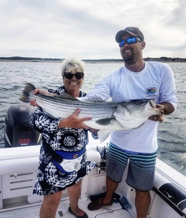 couple posing with striped bass on fishing charter in plymouth, ma