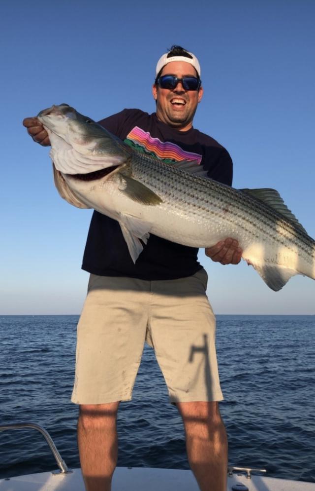 man in shorts posing with large striped bass