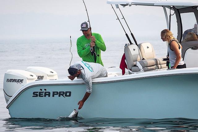 man leaning over the side of a boat to catch a fish