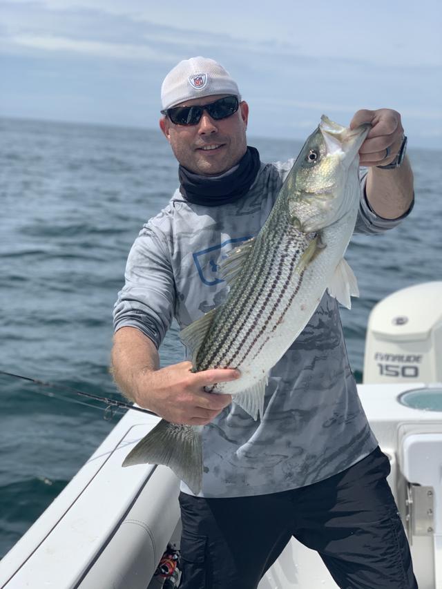 man showing off a striped bass with ocean in background
