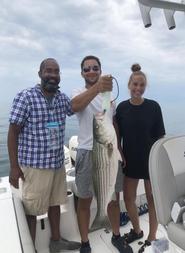 two men and a woman holding up a striped bass they caught on a fishing charter