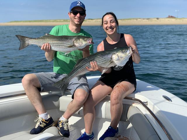 happy couple holding two striped bass on a fishing trip