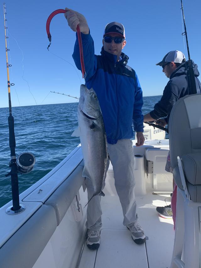 man in blue jacket holding a striped bass with the fishing line still in its mouth