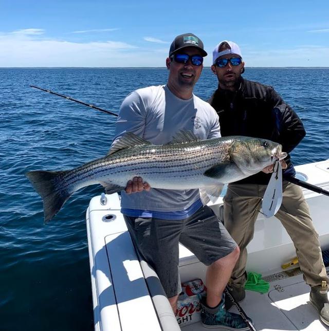 two men posing with fish at the back of a boat while deep sea fishing