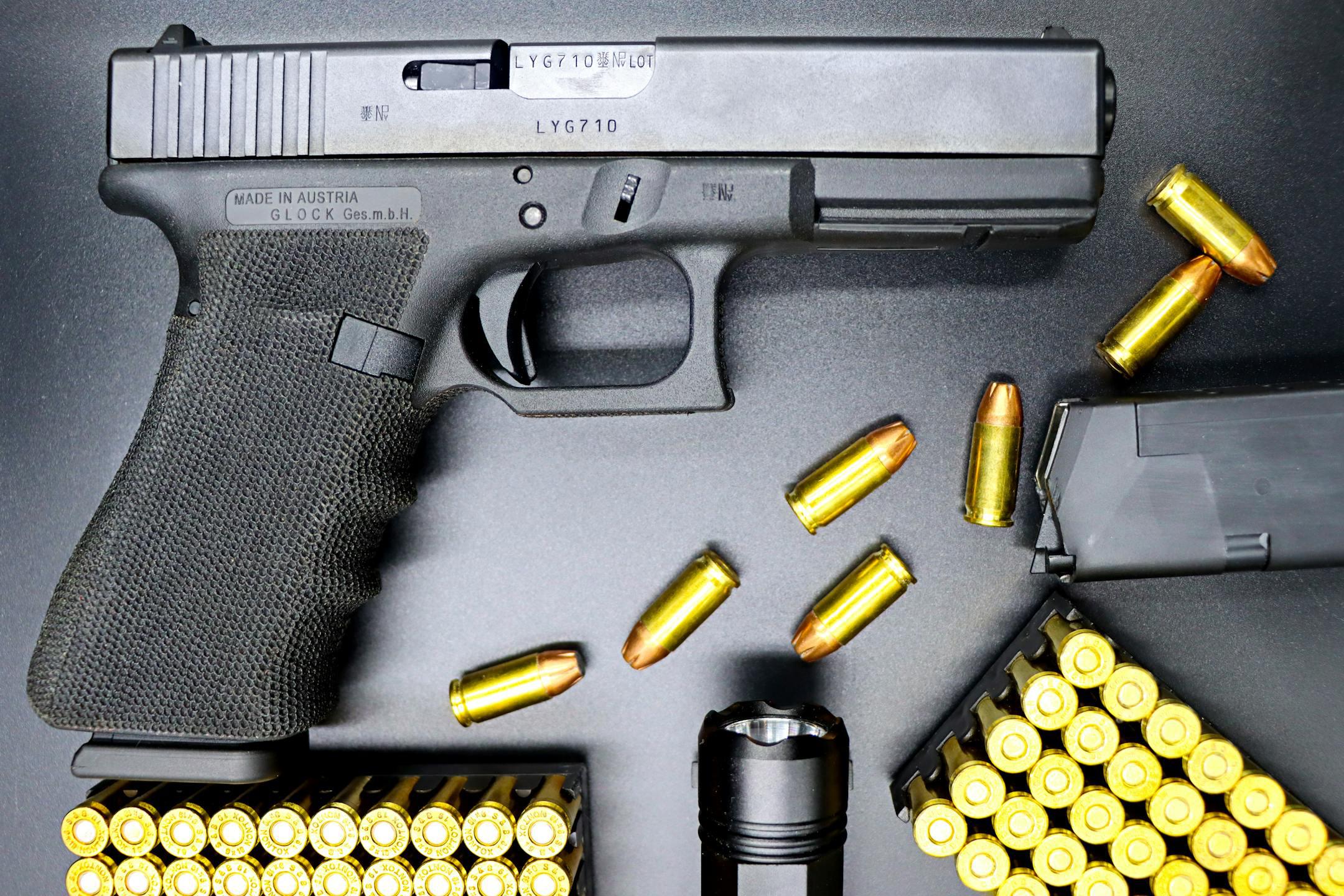 Top view of a Glock pistol, bullets, and flashlight on a black surface, showcasing firearms and ammunition.