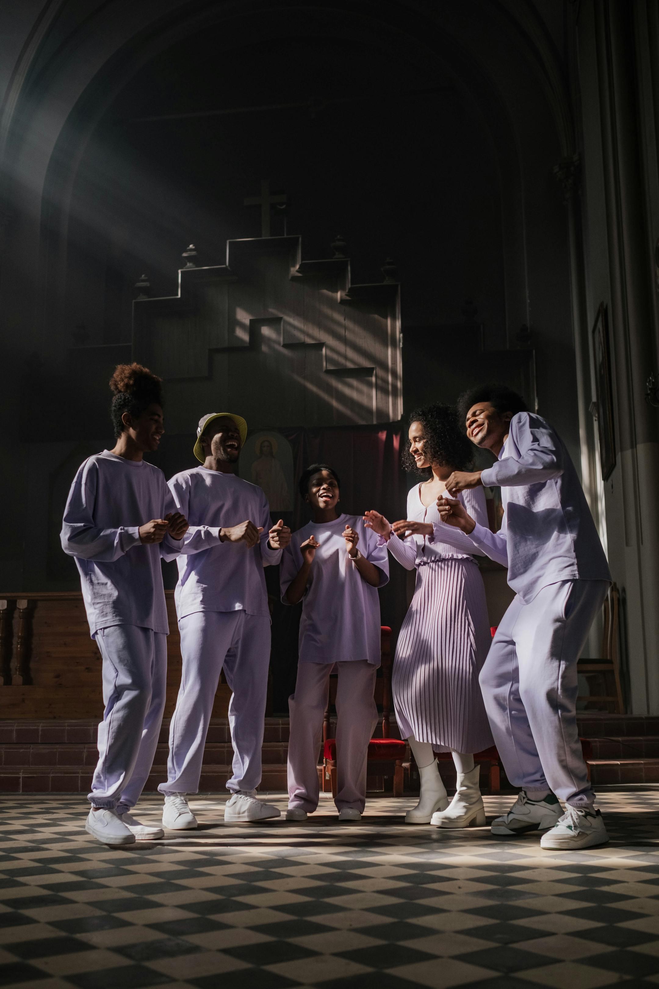 Group of young adults joyfully rehearsing music in a sunlit church setting.