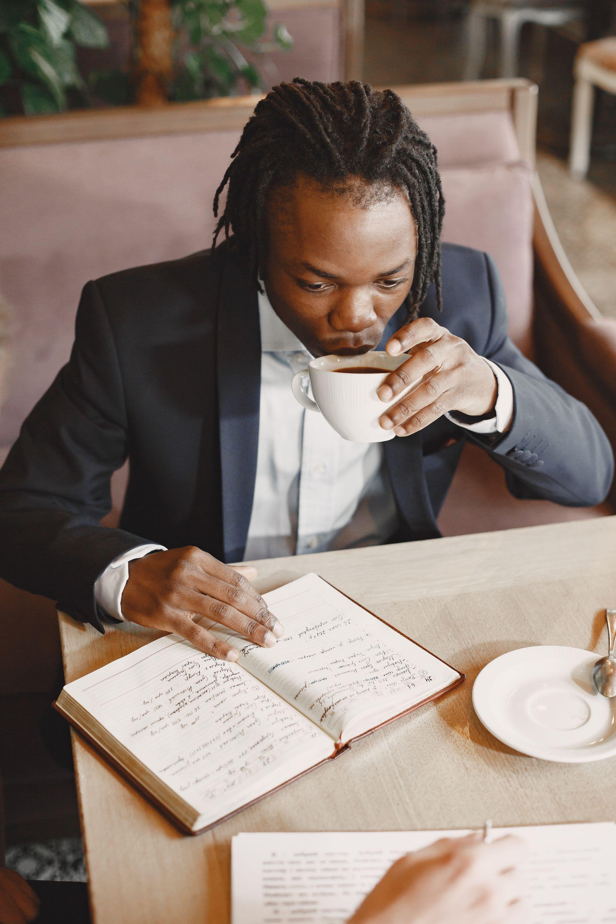 A businessman in a suit reads a book and enjoys coffee in a cozy cafe setting.