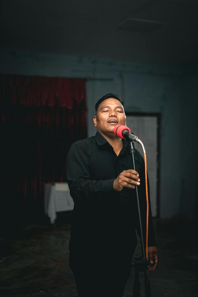 A man passionately singing into a microphone on stage indoors.
