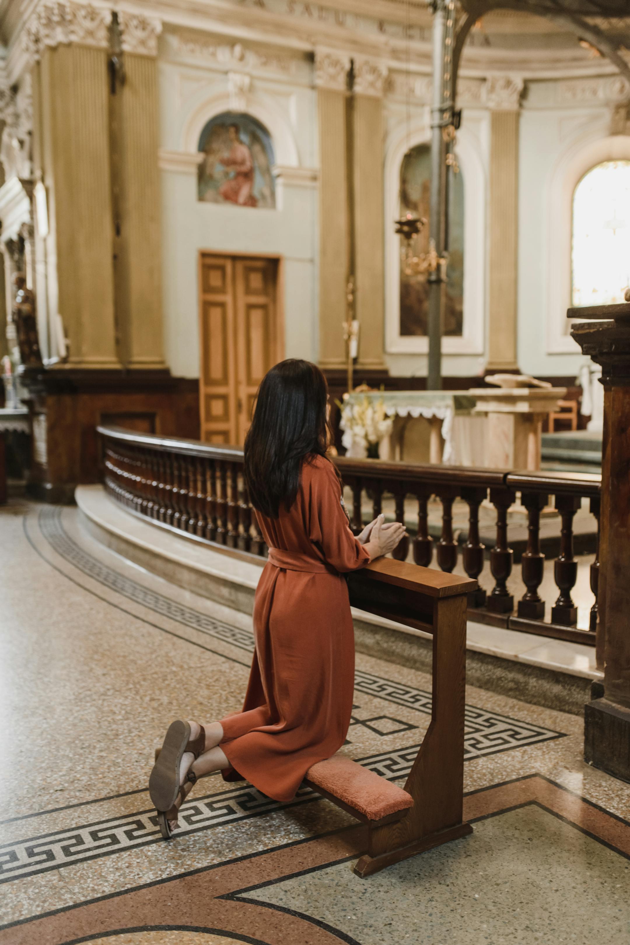 A woman kneels in prayer within an ornate church interior, showcasing faith and devotion.
