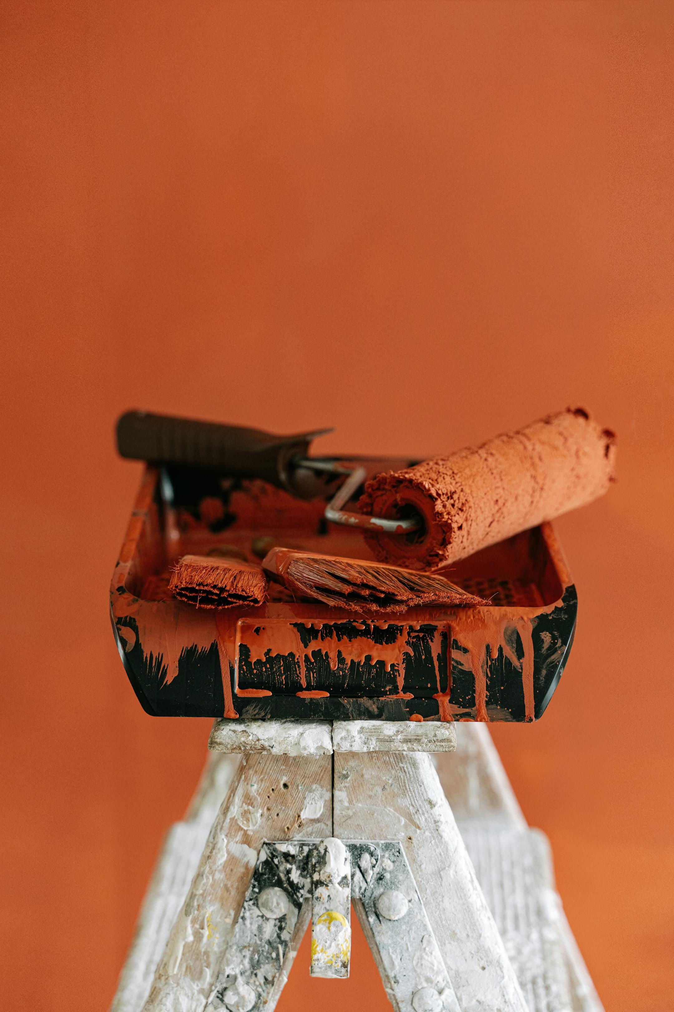A stepladder holds paint tools for a vibrant orange home renovation project.