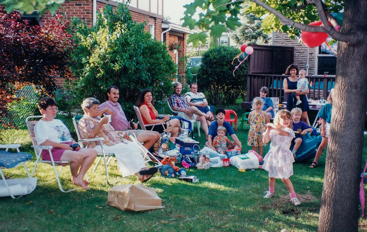 A joyful family gathering outdoors with children playing and adults relaxing in the backyard.