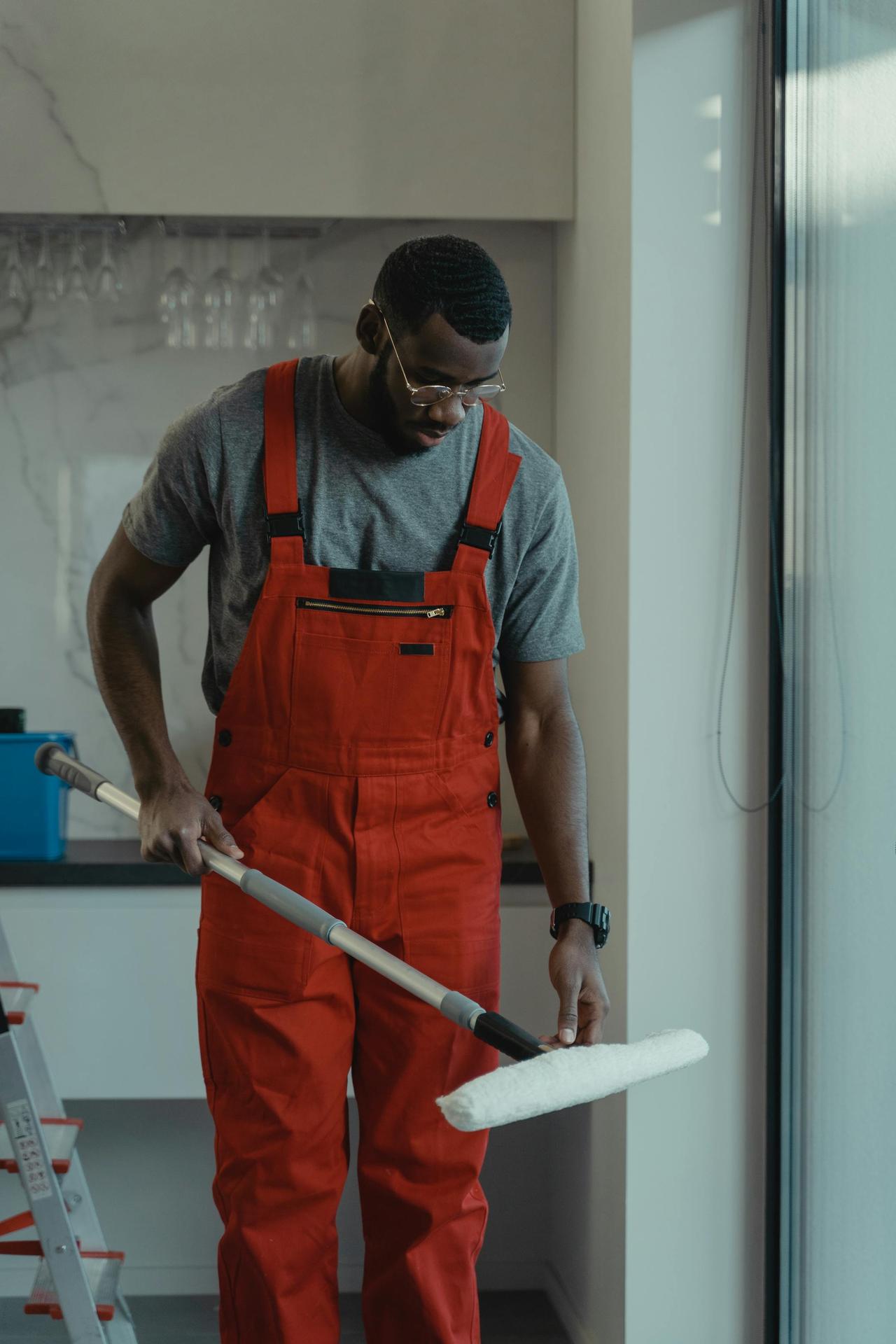 Man wearing red overalls using a mop indoors, depicting cleanliness and manual work.