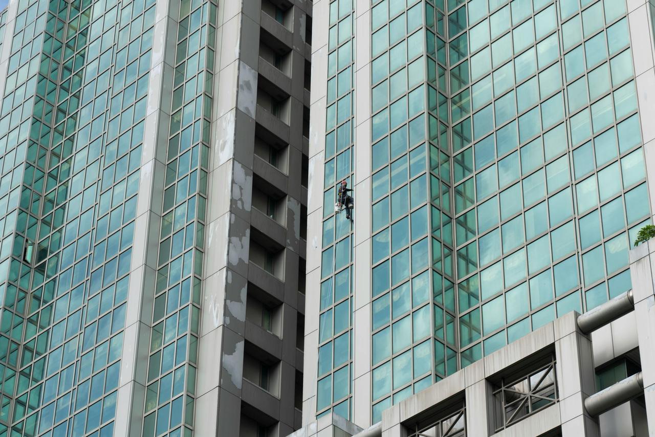 A worker cleans the glass windows of a tall skyscraper using harness and ropes.