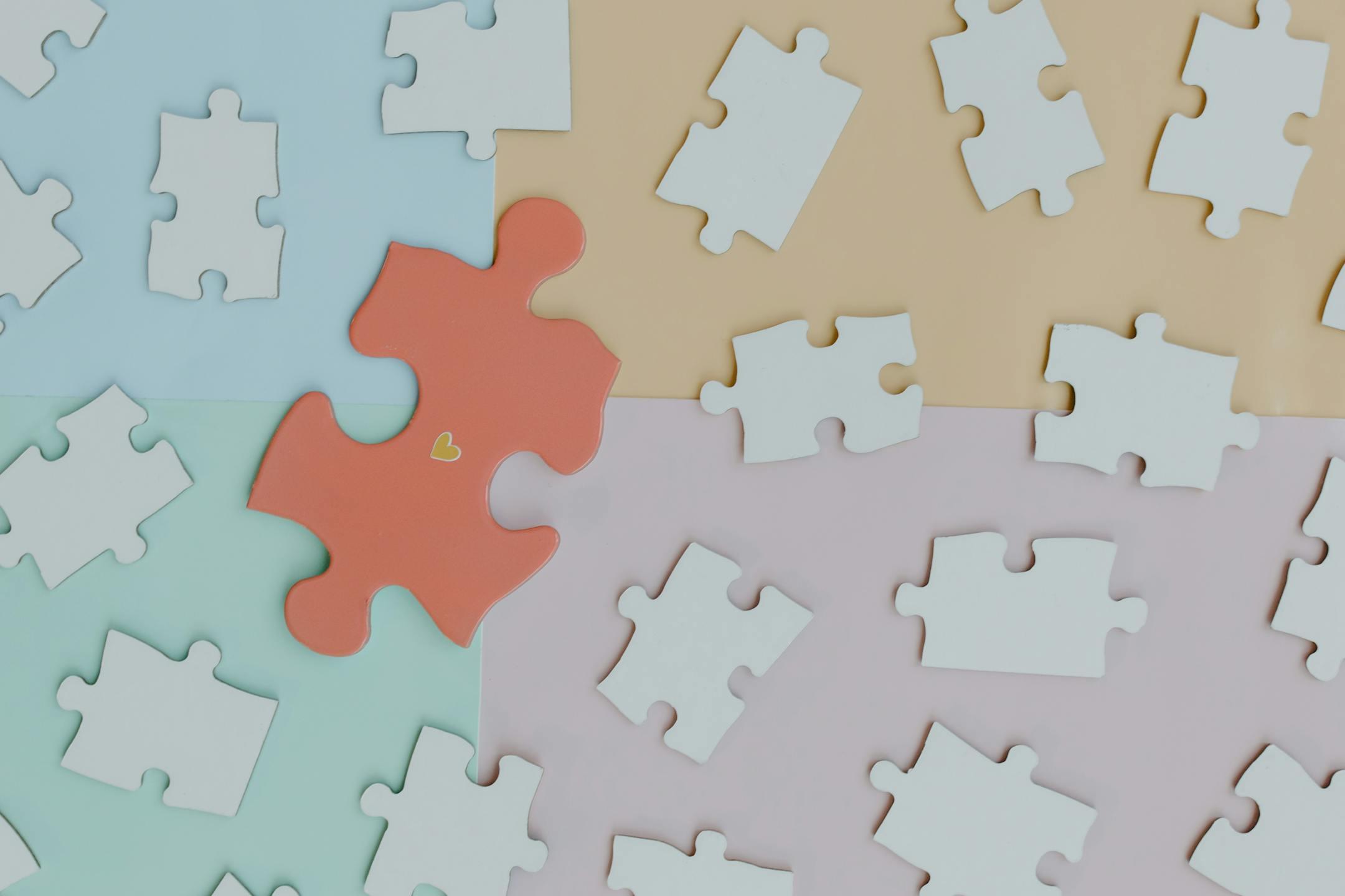 Close-up of scattered puzzle pieces on a pastel colored background, featuring a standout orange piece.