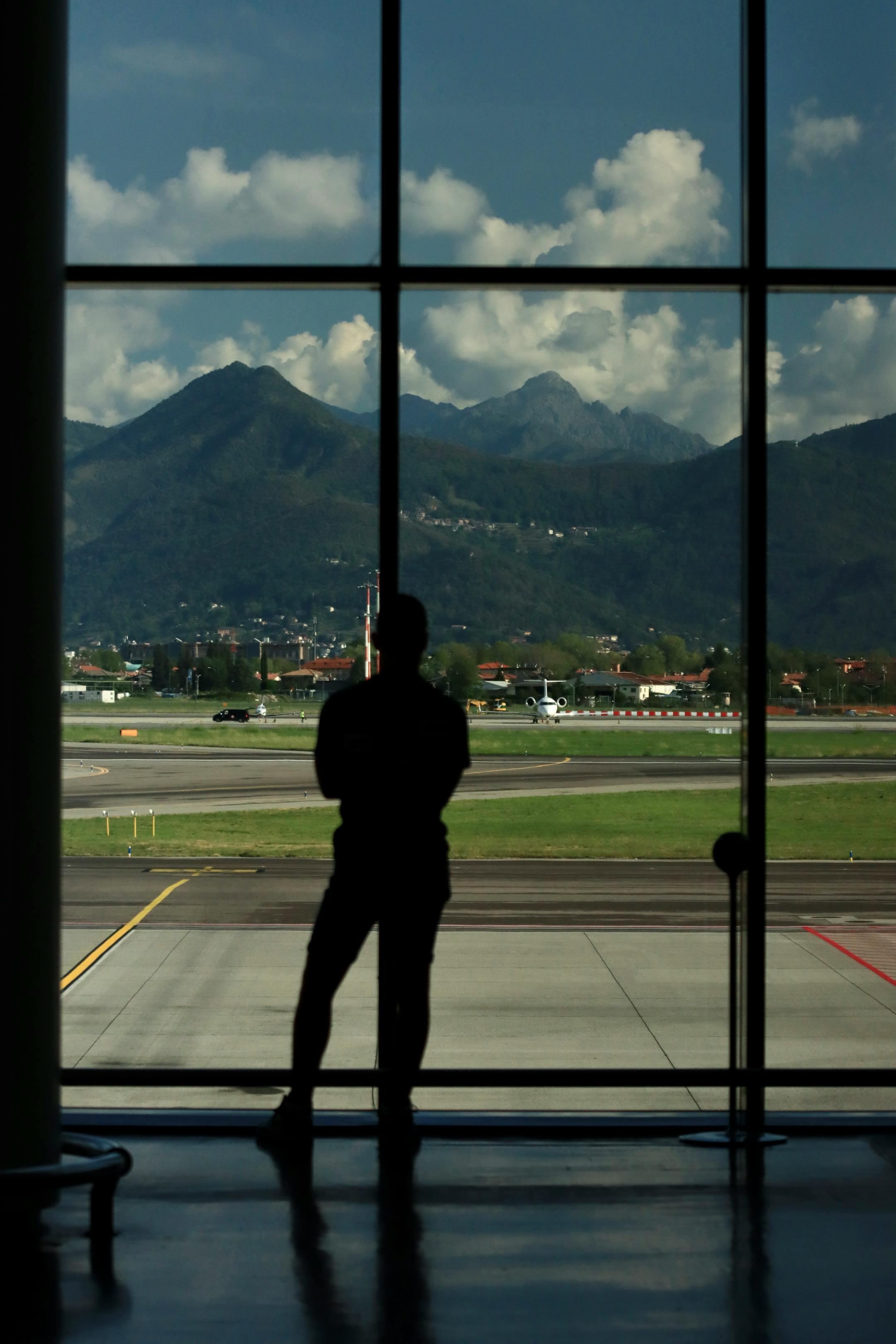 Silhouette of a person standing inside an airport terminal with a view of mountains in Lombardia, Italy.