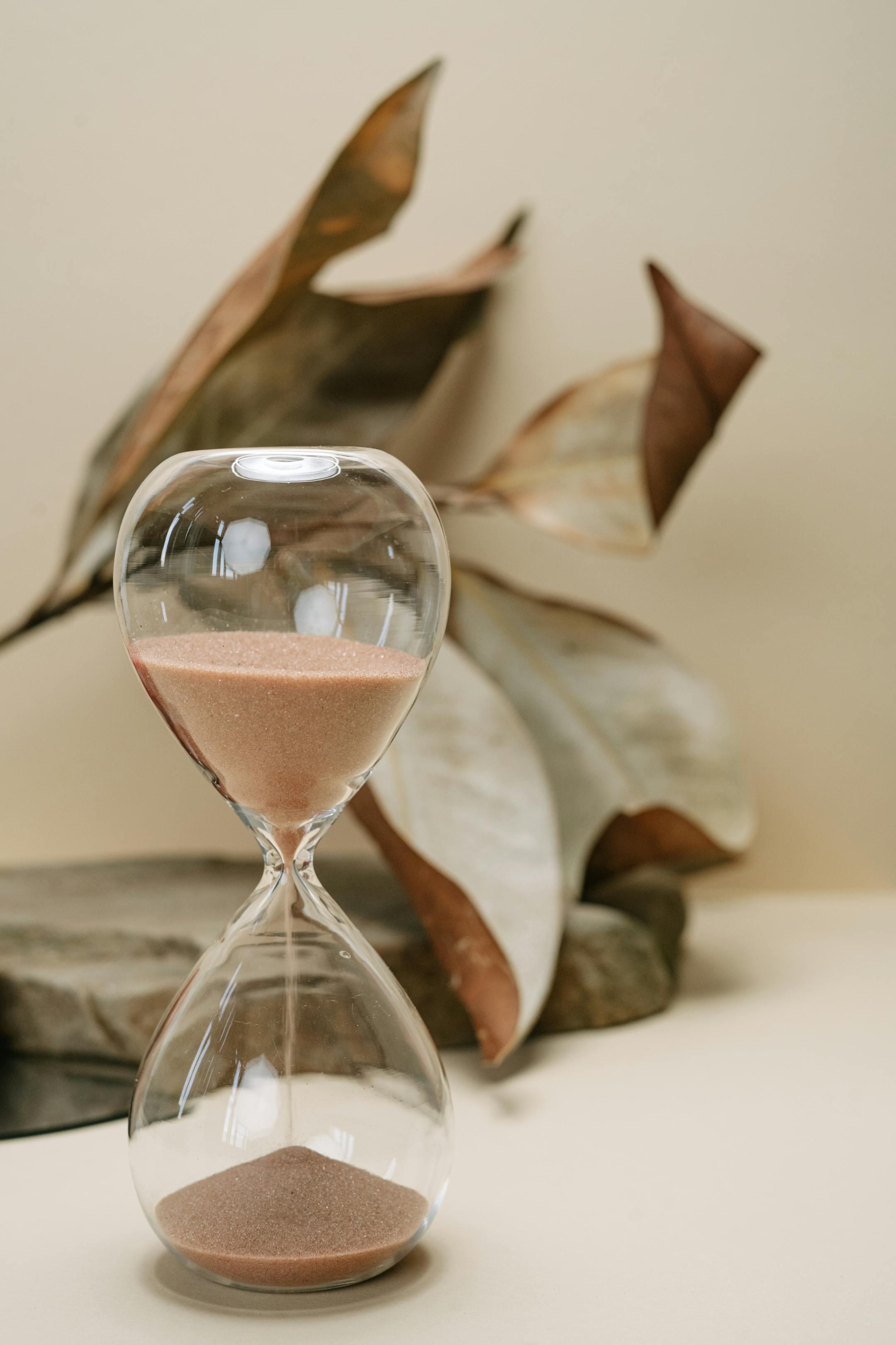 A still life photo of an hourglass with sand, set against dried leaves, symbolizing the passage of time.