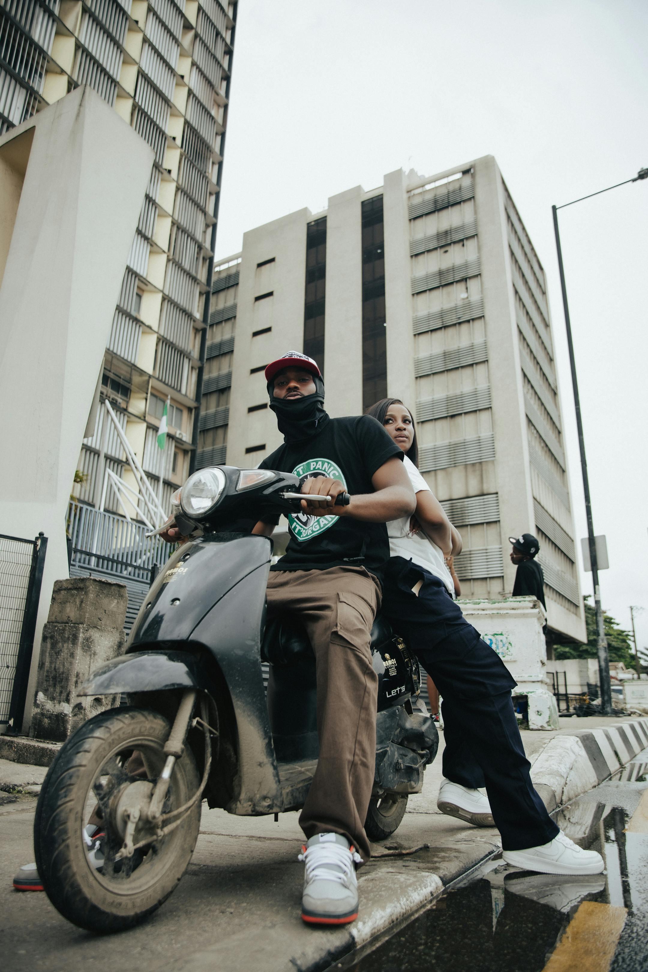 A stylish couple rides a scooter through the urban streets of Lagos, Nigeria.