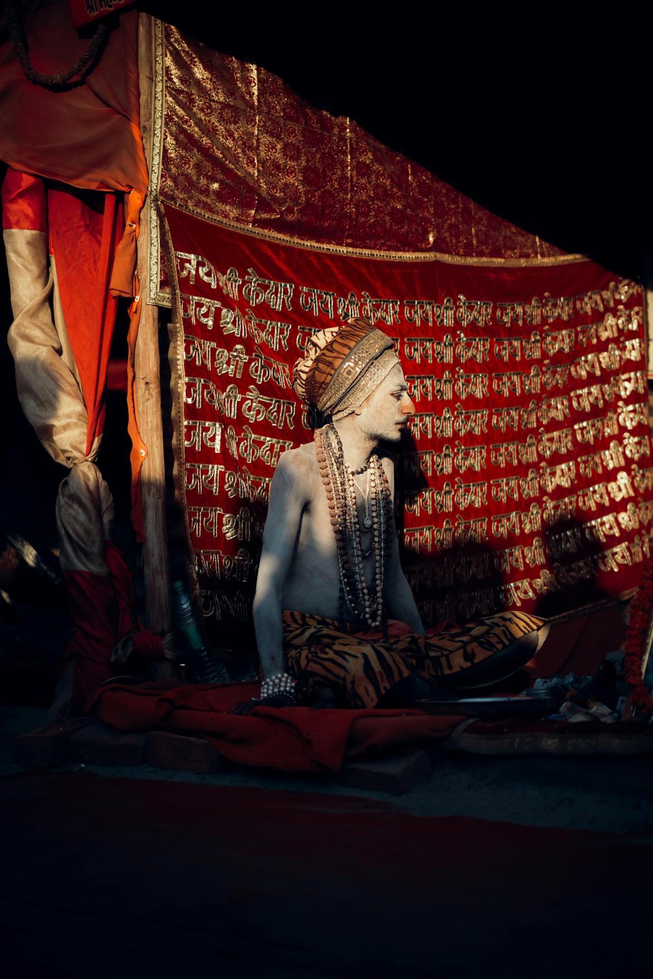 Sadhu meditating in colorful attire with traditional tent backdrop.