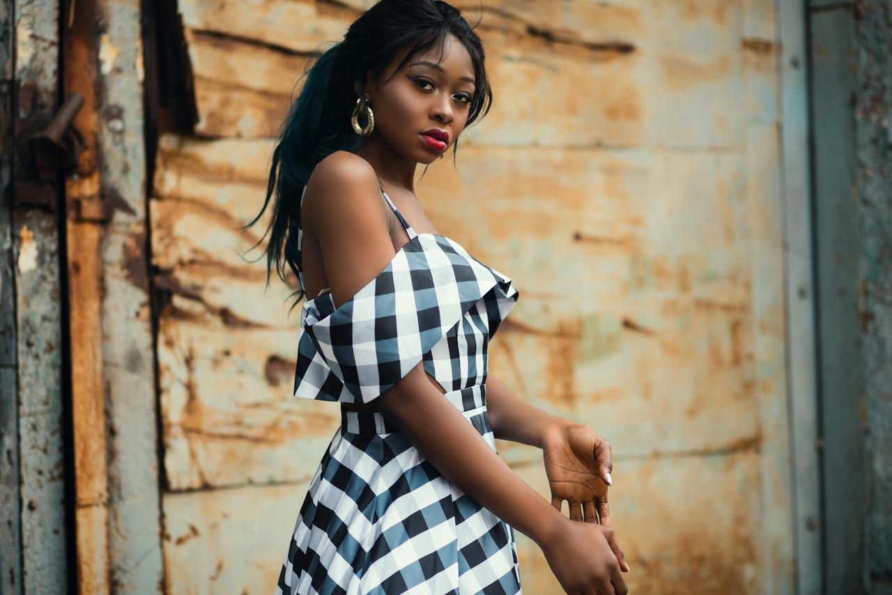 Elegant woman posing in a checkered dress against a rustic background.