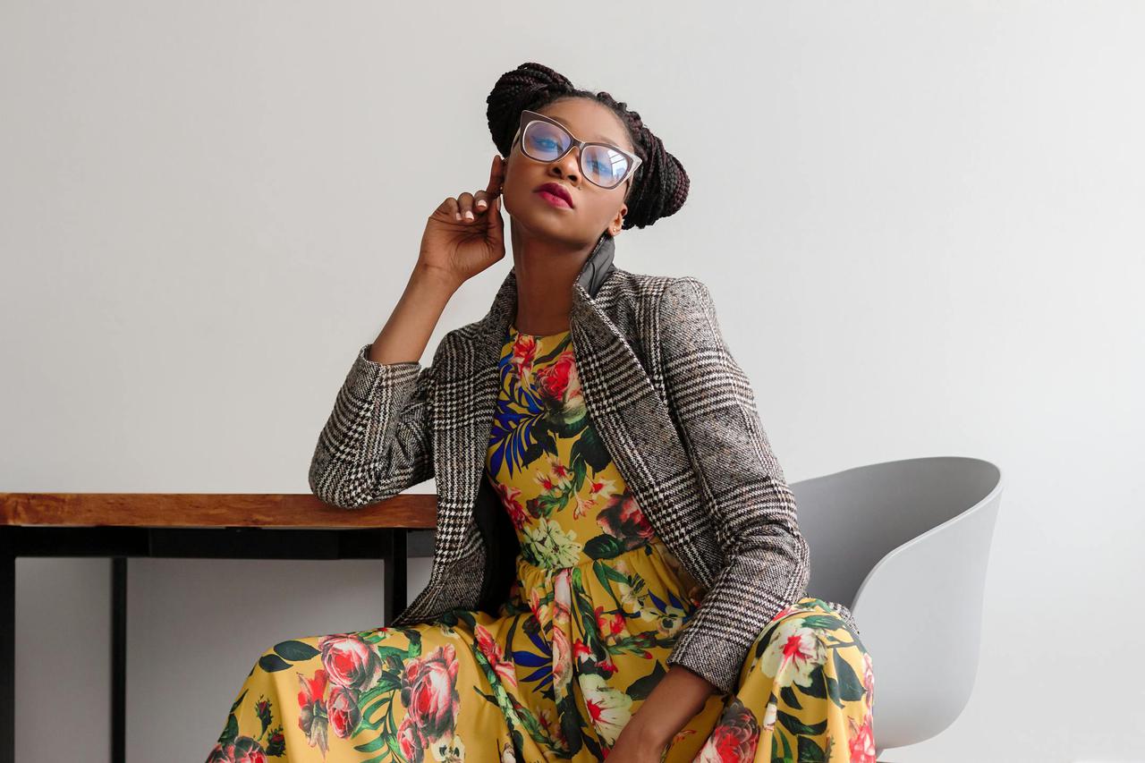 Elegant woman posing in a modern setting, wearing a floral dress and eyeglasses.