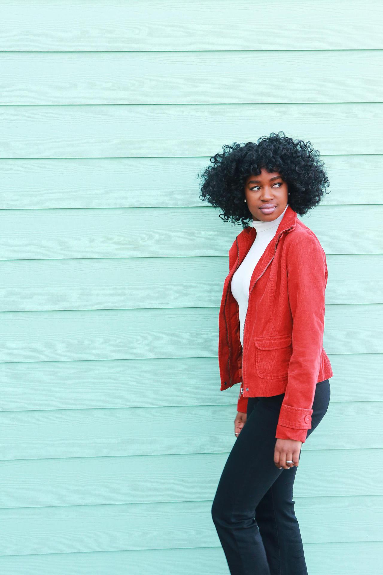 Fashionable woman in a red jacket posing against a mint green wall, showcasing vibrant street style.