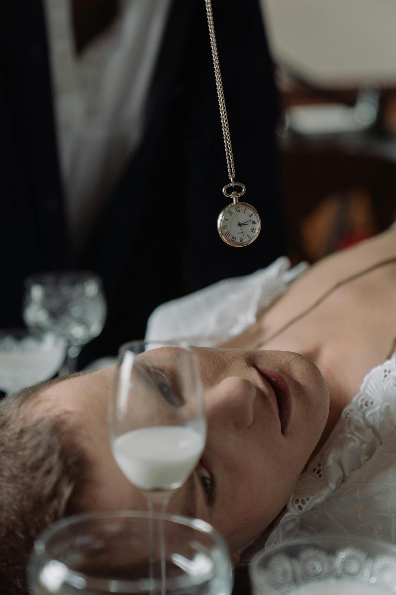 A man in a mesmerizing pose with a swinging pocket watch and wine glass, creating a cinematic effect.