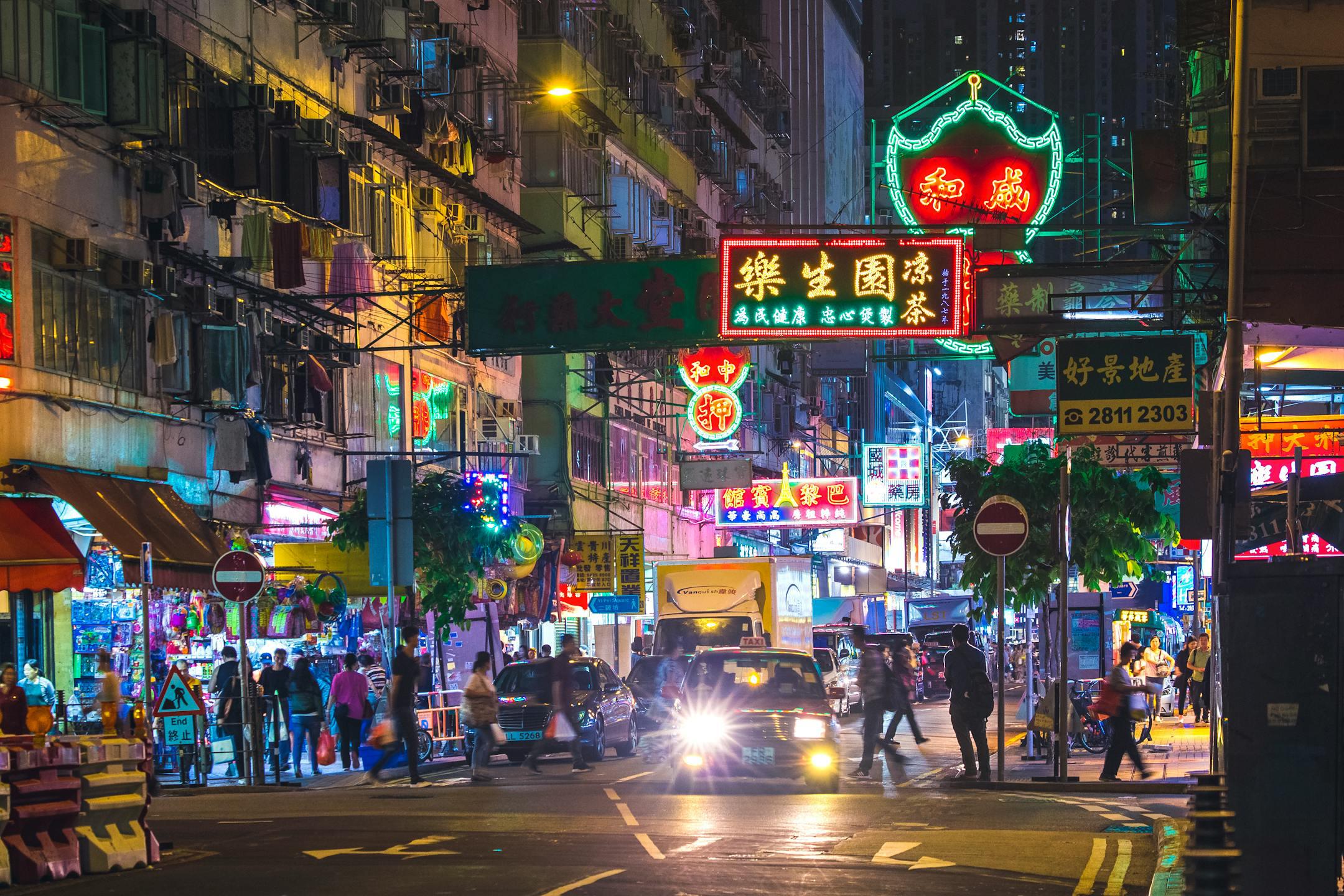 Colorful neon lights illuminate a bustling street in the New Territories, Hong Kong, by night.