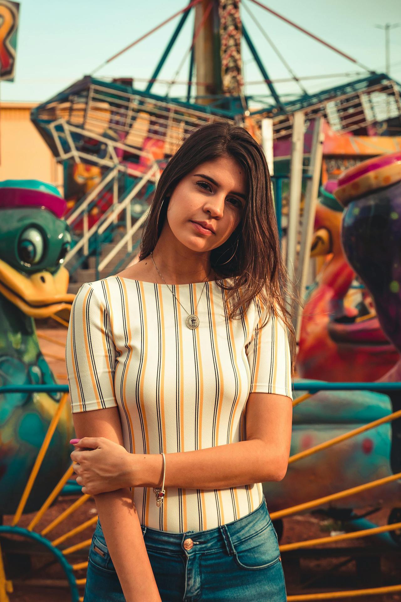Young woman posing confidently at a vibrant amusement park. Perfect for fashion and lifestyle projects.
