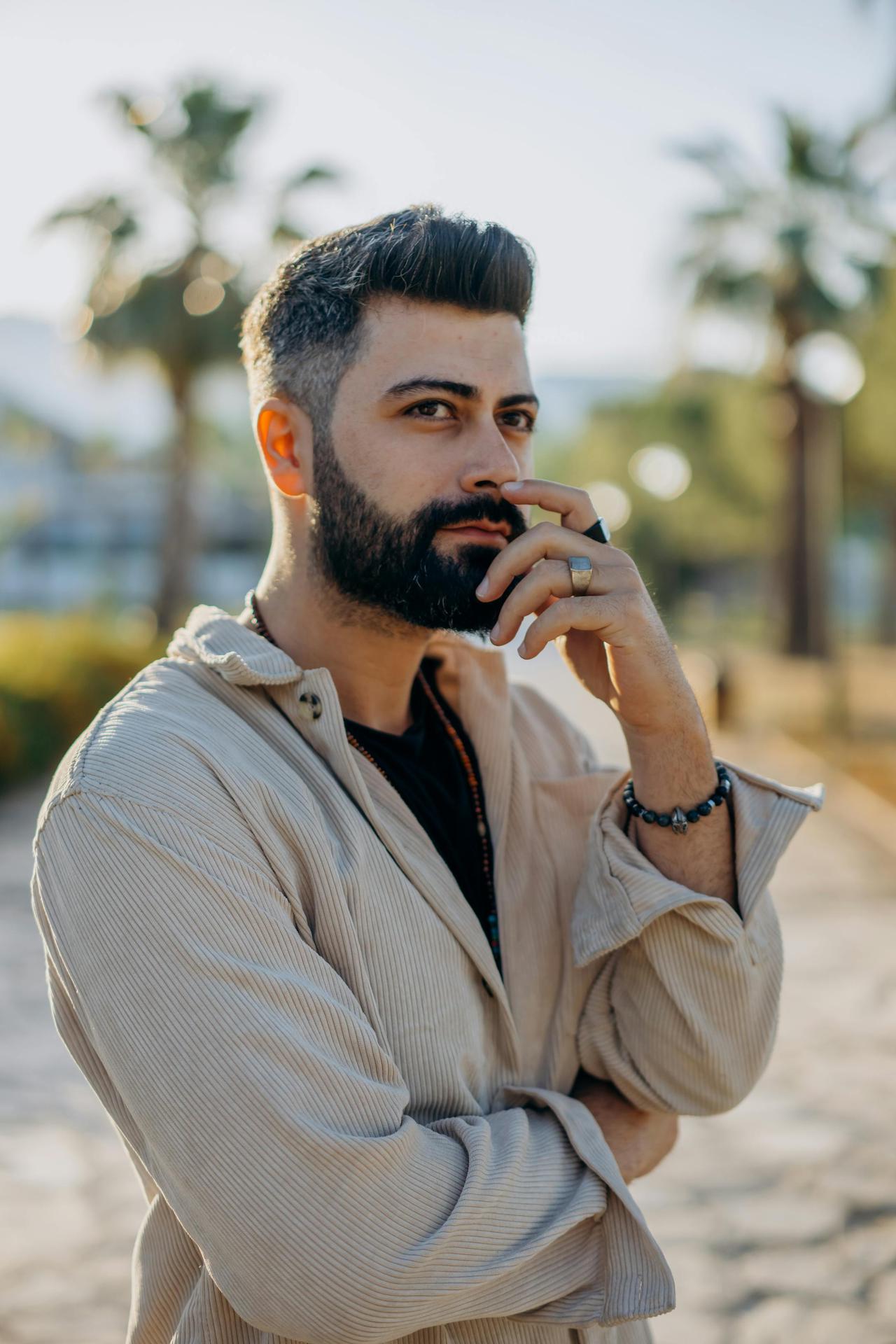 A thoughtful man with facial hair poses outdoors, framed by palm trees in warm sunlight.