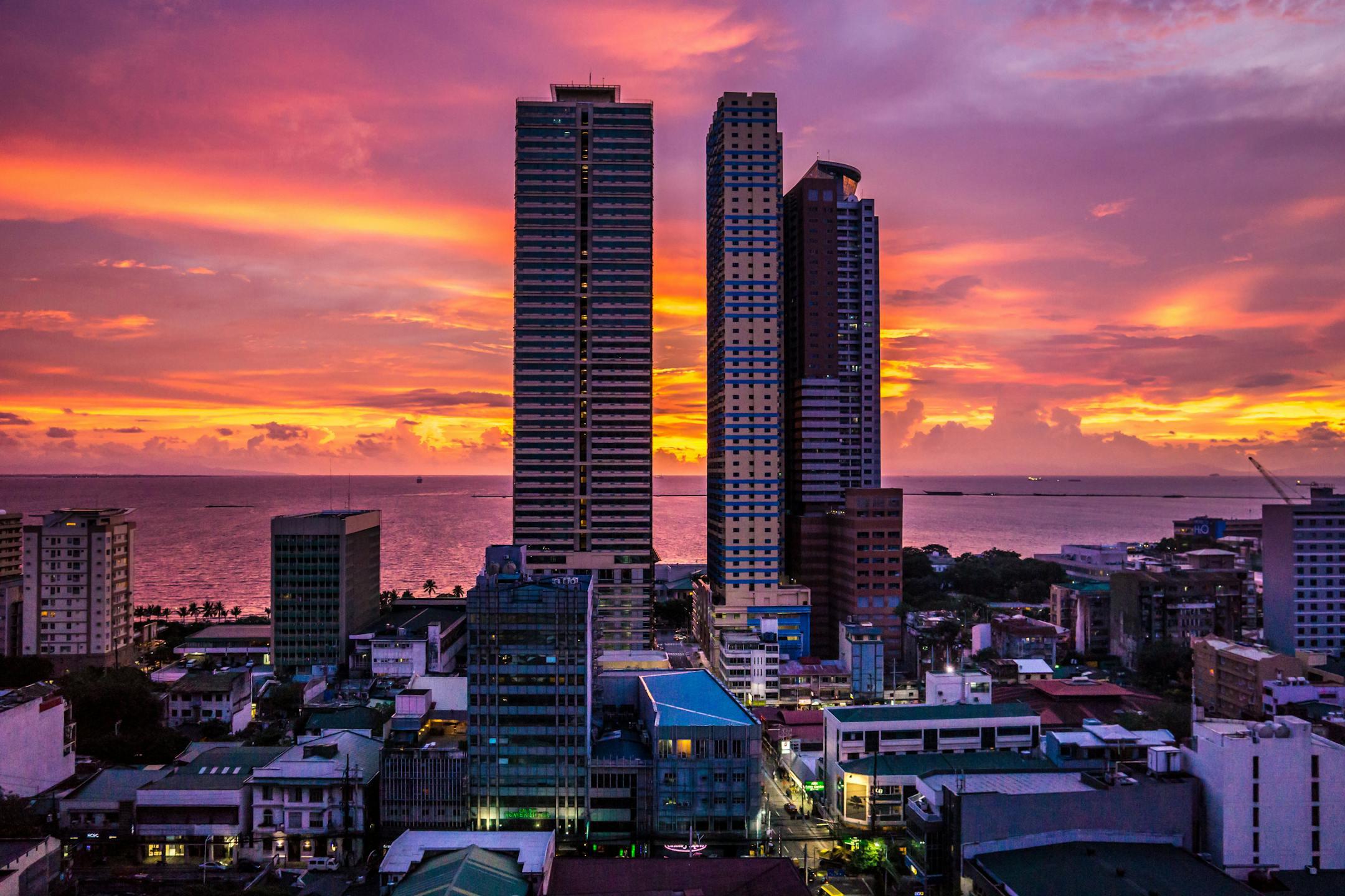 Stunning cityscape of Manila skyscrapers during a colorful sunset with sea view.